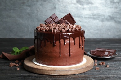 Photo of Freshly made delicious chocolate cake on black wooden table against grey background