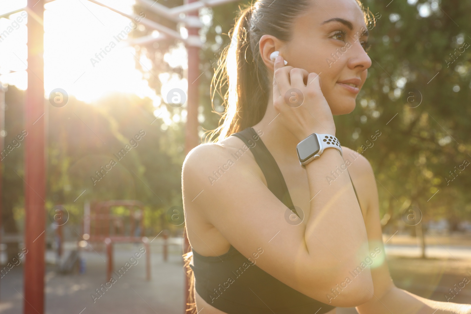Photo of Woman wearing modern smart watch and earphones during training outdoors