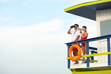 Lifeguards with megaphone and binocular on watch tower against blue sky