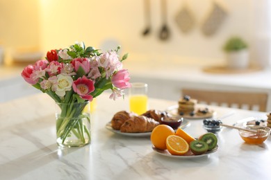 Bouquet of beautiful flowers in vase and food for breakfast on white marble table