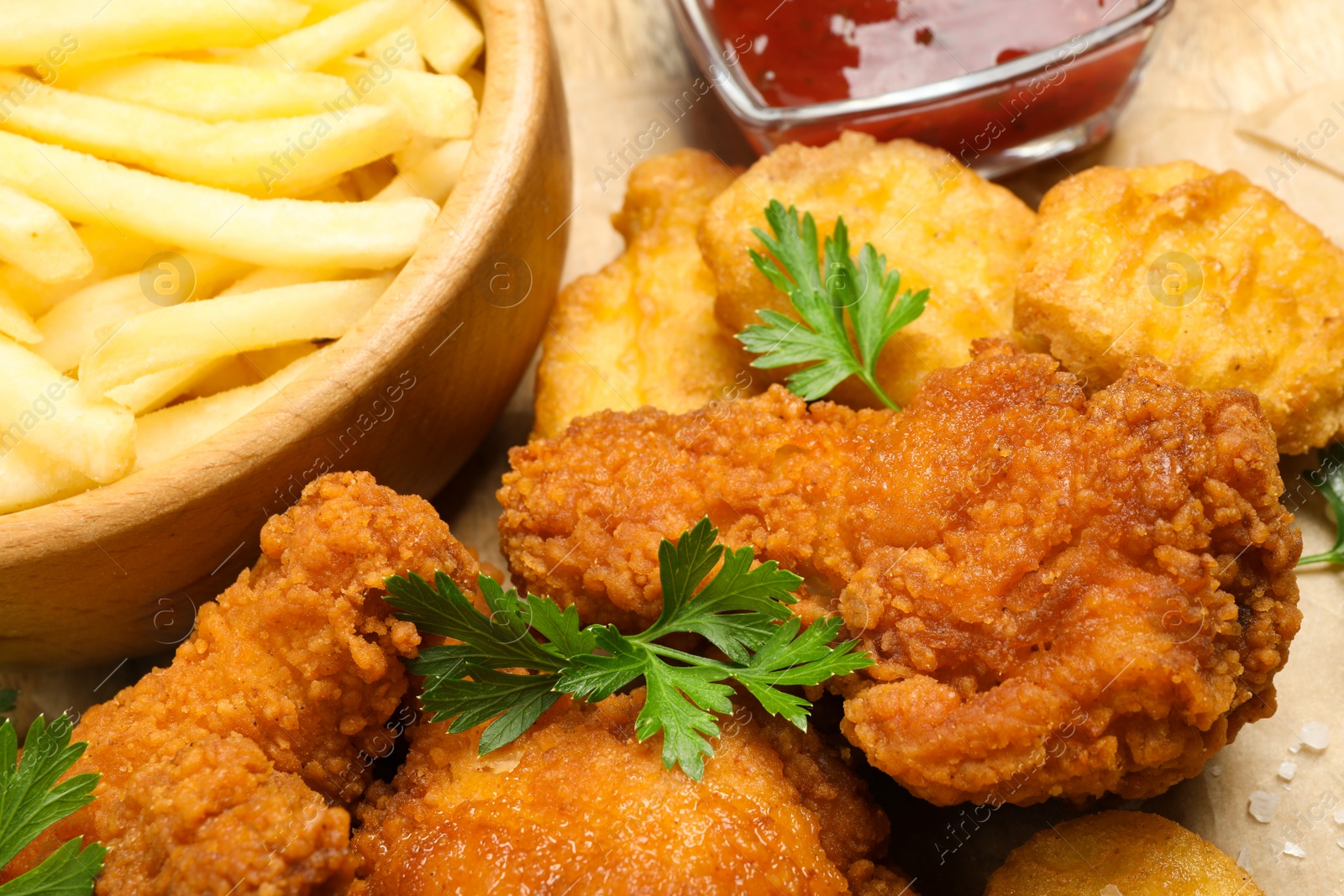 Photo of Tasty deep fried chicken pieces and nuggets on parchment, closeup