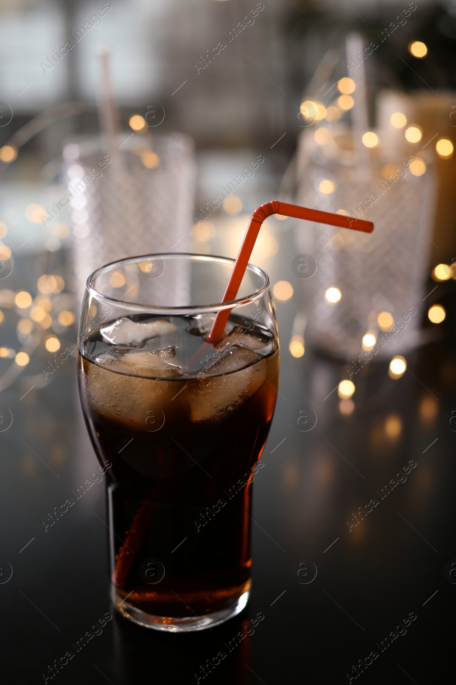 Photo of Glass of cold cola and fairy lights on table