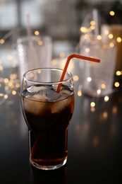 Photo of Glass of cold cola and fairy lights on table