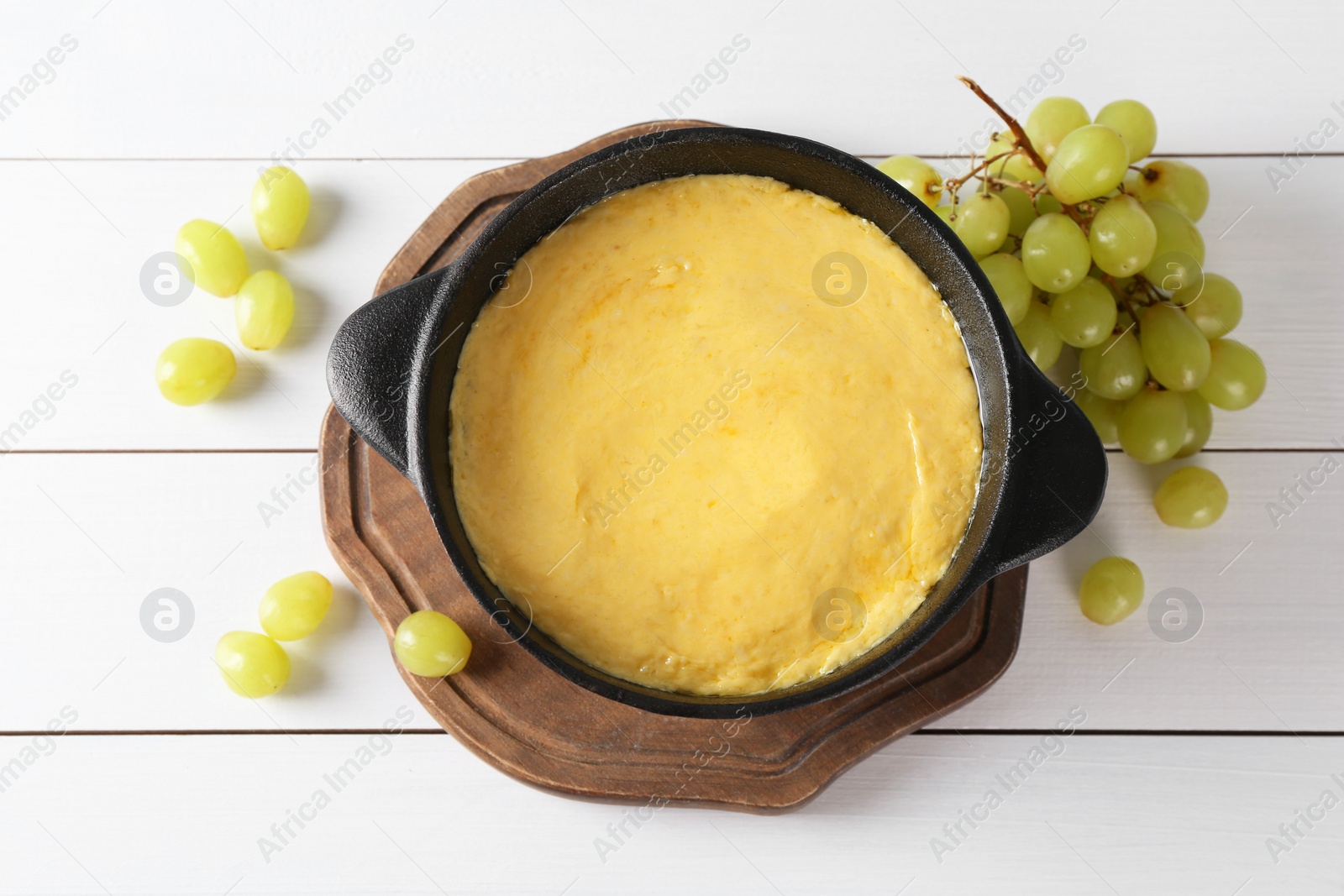 Photo of Fondue with tasty melted cheese and grapes on white wooden table, flat lay