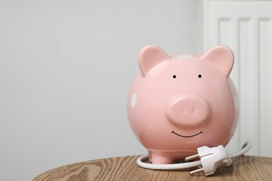 Photo of Piggy bank and plug on wooden table near heating radiator, space for text