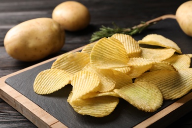 Photo of Board with crispy potato chips on wooden table