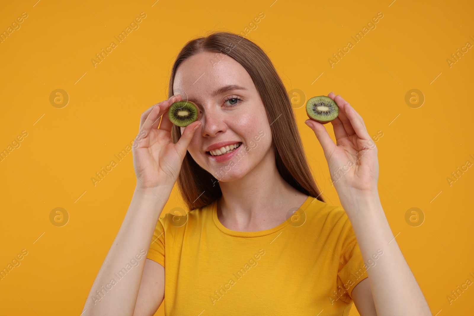 Photo of Young woman holding halves of kiwi on yellow background