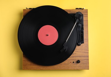 Photo of Modern vinyl record player with disc on yellow background, top view