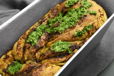 Photo of Freshly baked pesto bread in loaf pan on table, closeup