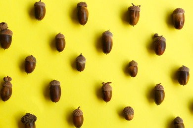 Photo of Many acorns on yellow background, flat lay
