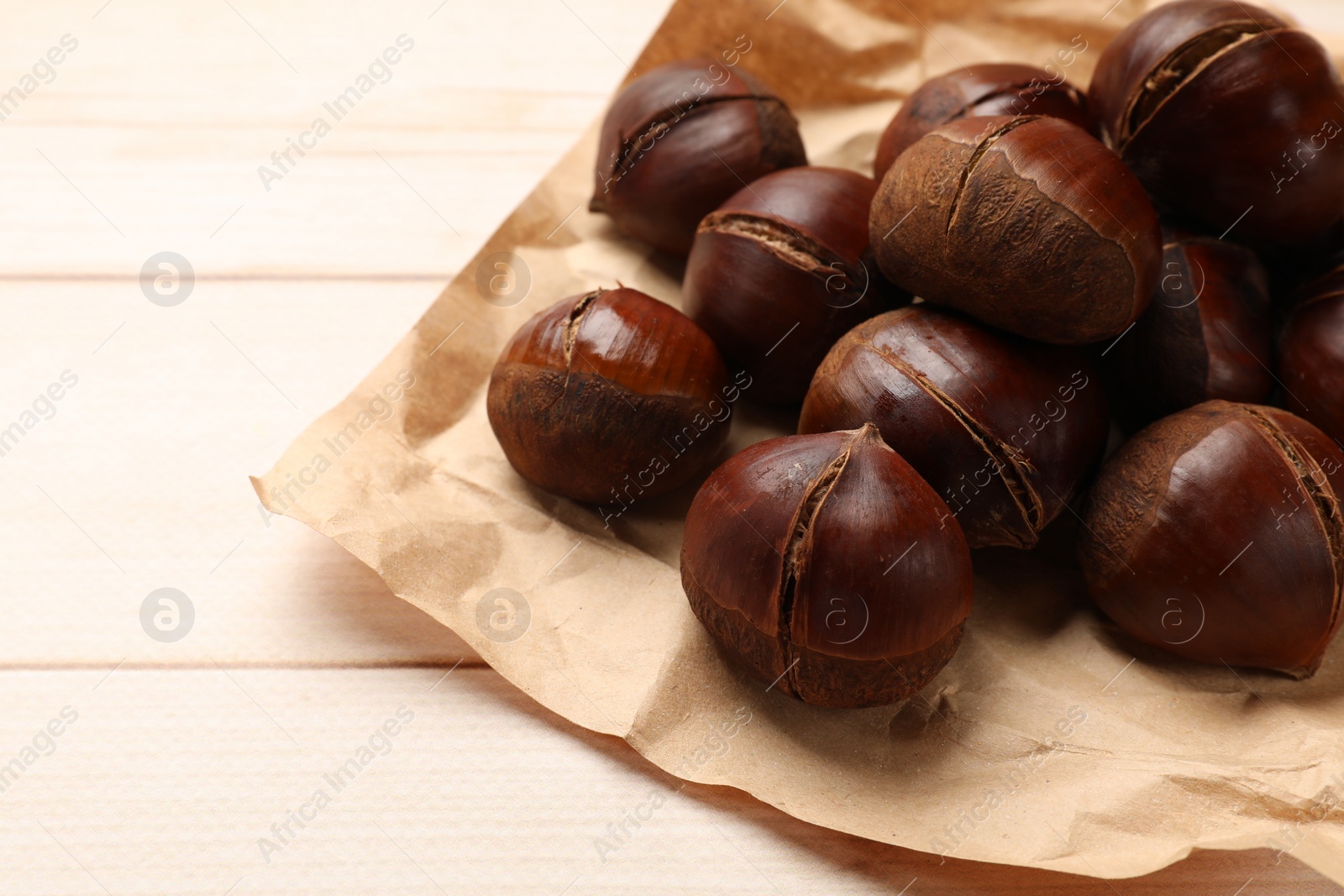 Photo of Roasted edible sweet chestnuts on wooden table, space for text