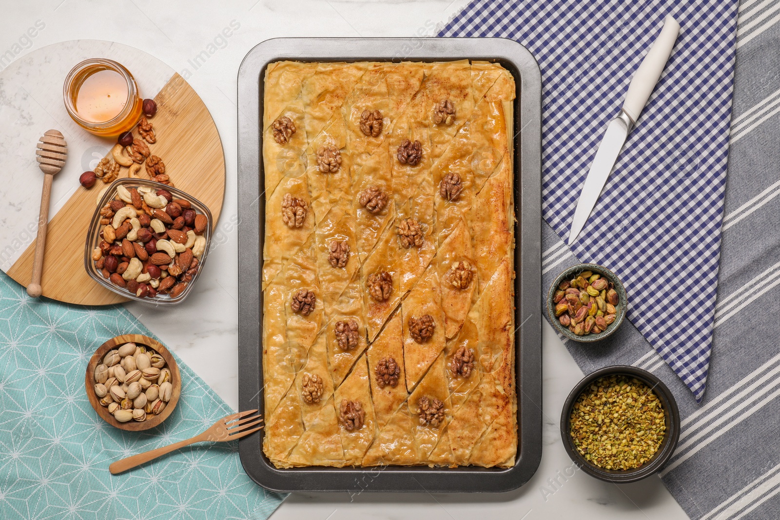 Photo of Delicious baklava with walnuts in baking pan, honey and nuts on white table, flat lay