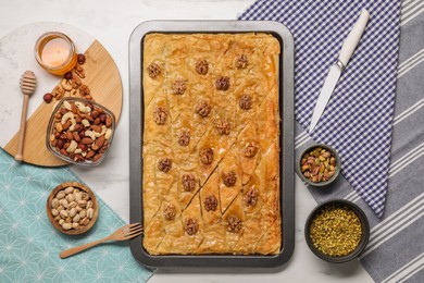 Delicious baklava with walnuts in baking pan, honey and nuts on white table, flat lay