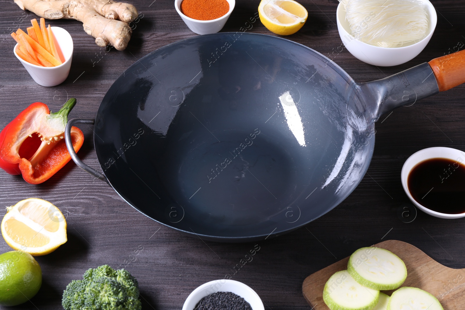 Photo of Empty iron wok surrounded by ingredients on dark grey wooden table