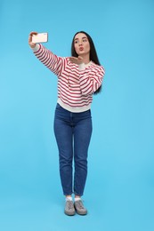 Photo of Young woman taking selfie with smartphone and blowing kiss on light blue background