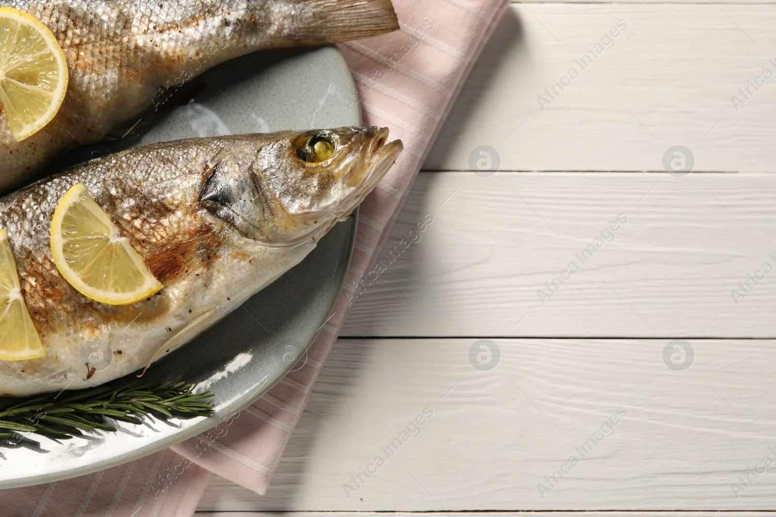 Photo of Delicious baked fish, lemon and rosemary on white wooden table, top view. Space for text