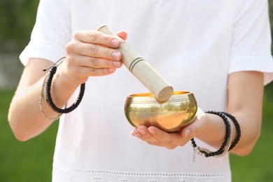 Photo of Woman using singing bowl in sound healing therapy outdoors, closeup