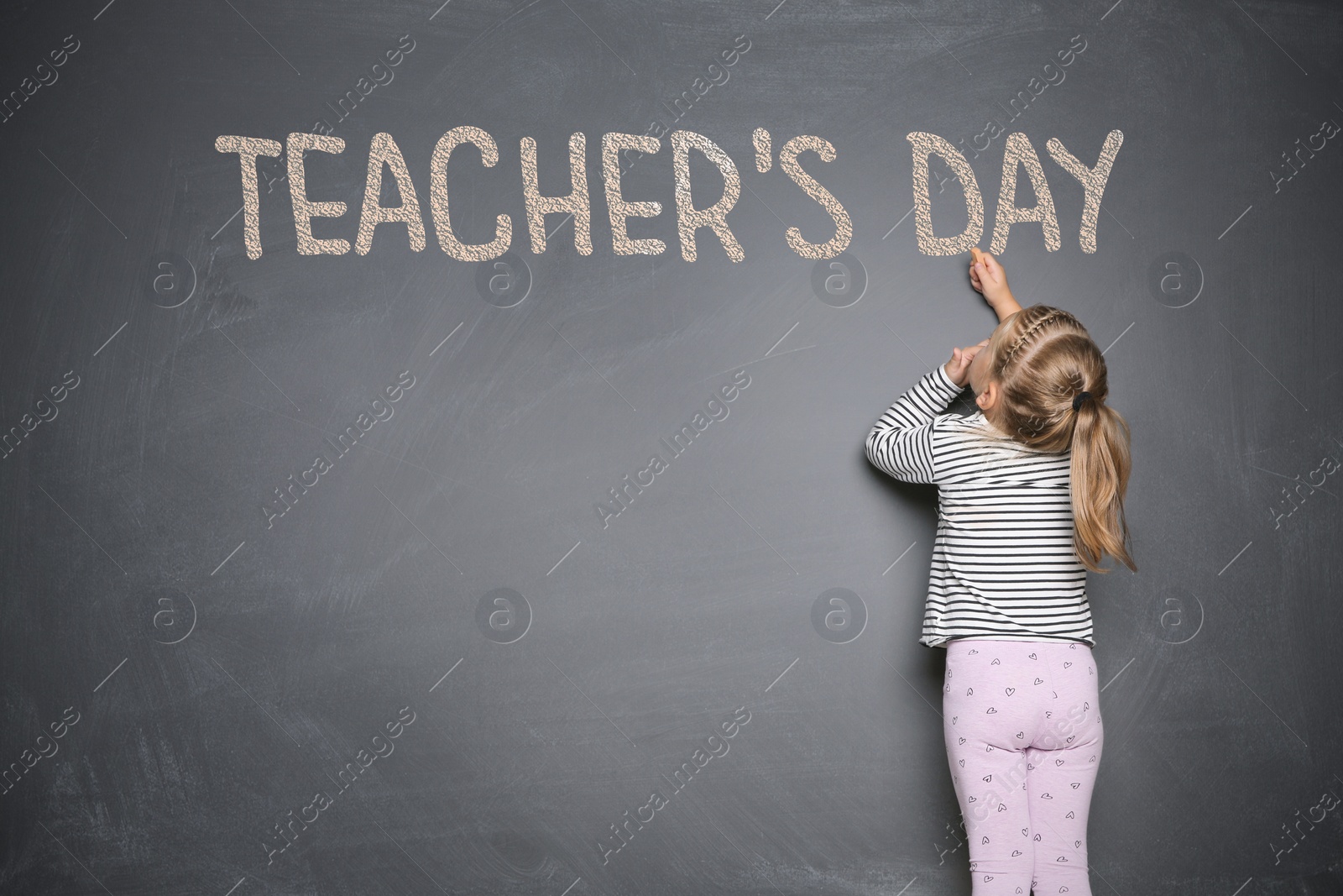 Image of Cute little girl writing phrase Teacher's Day with chalk on blackboard