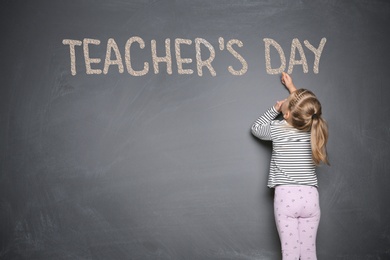 Image of Cute little girl writing phrase Teacher's Day with chalk on blackboard