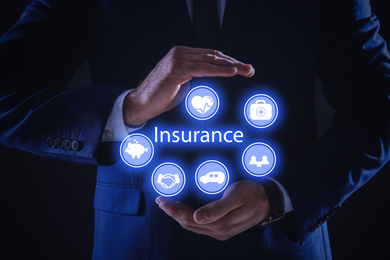 Image of Businessman holding different icons on dark background, closeup. Insurance concept
