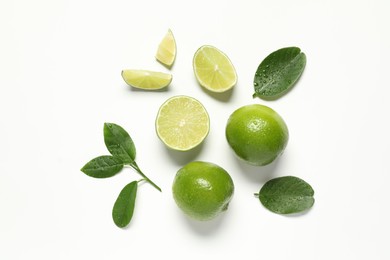 Photo of Whole and cut fresh ripe limes with green leaves on white background, flat lay