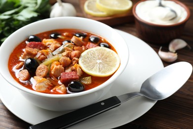 Photo of Meat solyanka soup with sausages, olives and vegetables served on wooden table, closeup