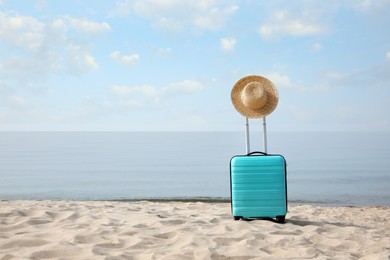 Photo of Turquoise suitcase with straw hat on sandy beach, space for text