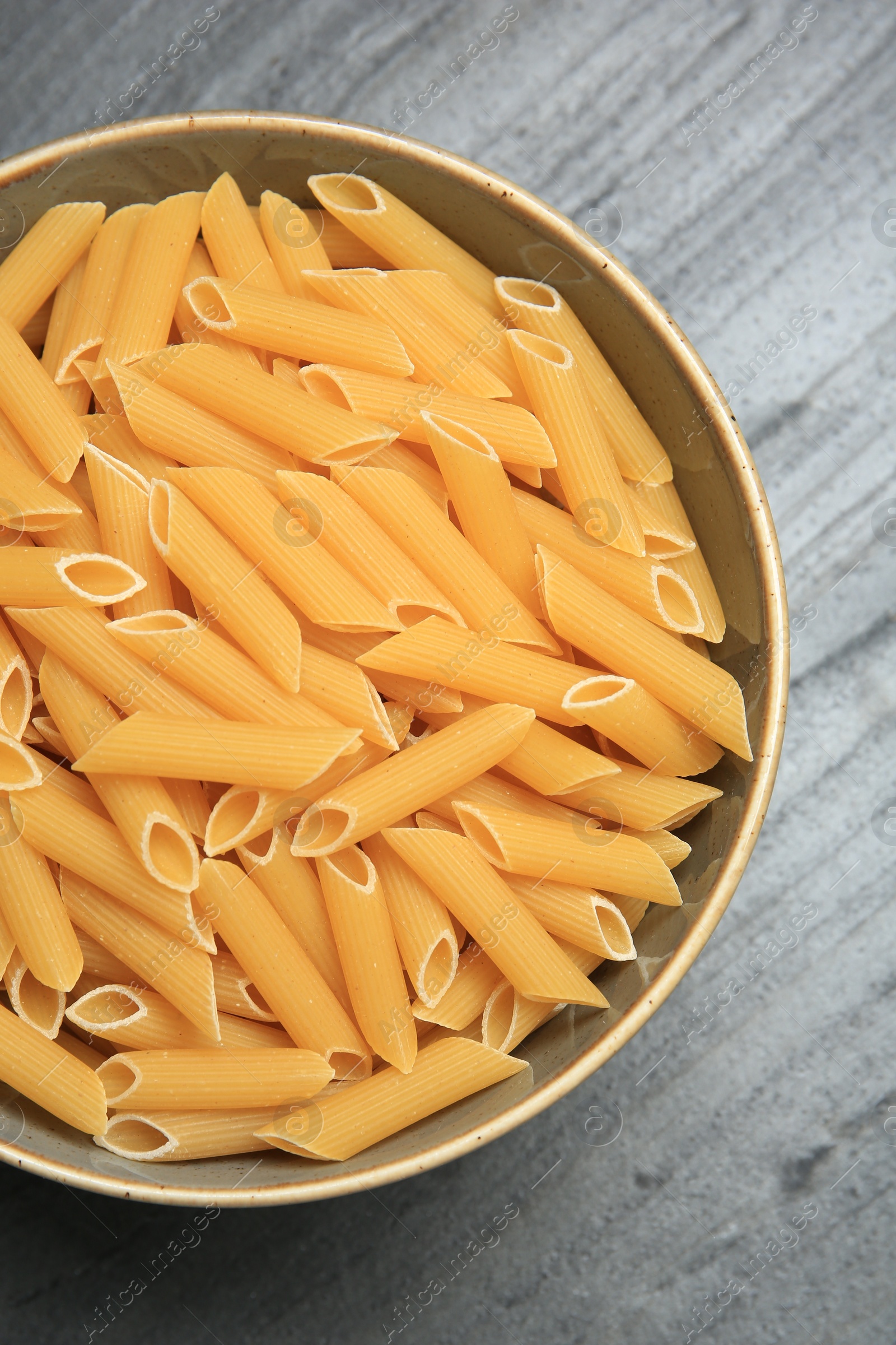 Photo of Raw penne pasta in bowl on grey table, top view