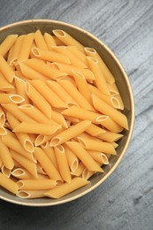 Photo of Raw penne pasta in bowl on grey table, top view