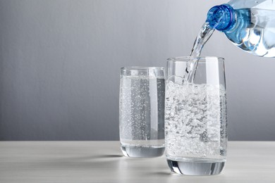 Photo of Pouring soda water from bottle into glass on grey background. Space for text