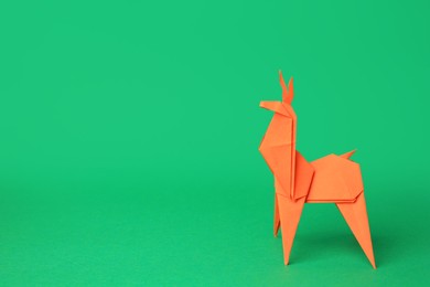 Photo of Origami art. Handmade orange paper deer on green background, space for text