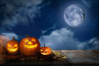 Image of Spooky pumpkin head jack lanterns under full moon on Halloween. Space for text