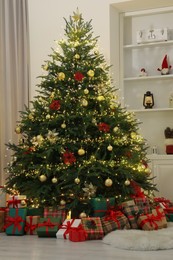 Photo of Many gift boxes under Christmas tree decorated with ornaments and festive lights in room