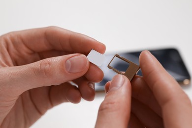 Woman with SIM card and slot tray on white background, closeup