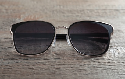 Stylish sunglasses on wooden background, closeup view
