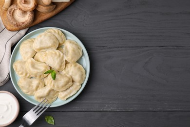 Photo of Plate of delicious dumplings (varenyky) with mushrooms on grey wooden table, flat lay. Space for text
