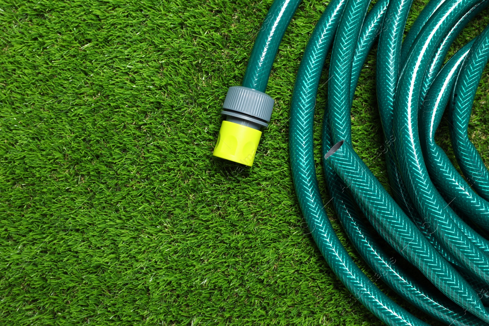 Photo of Watering hose on green grass, top view. Space for text