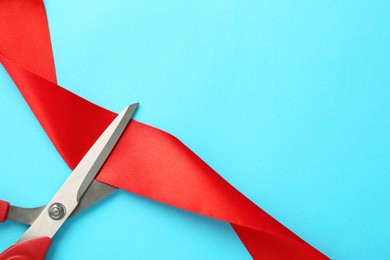 Red ribbon and scissors on light blue background, top view. Space for text