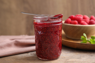 Delicious jam and fresh raspberries on wooden table, closeup