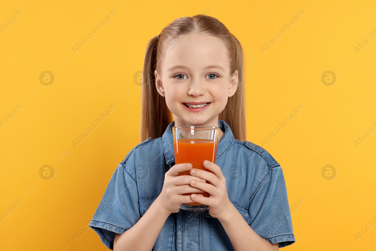 Photo of Cute little girl with glass of fresh juice on orange background, space for text