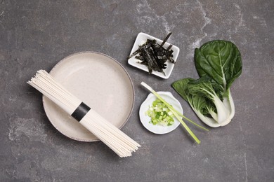 Photo of Cooking delicious ramen soup. Different ingredients on gray table, flat lay