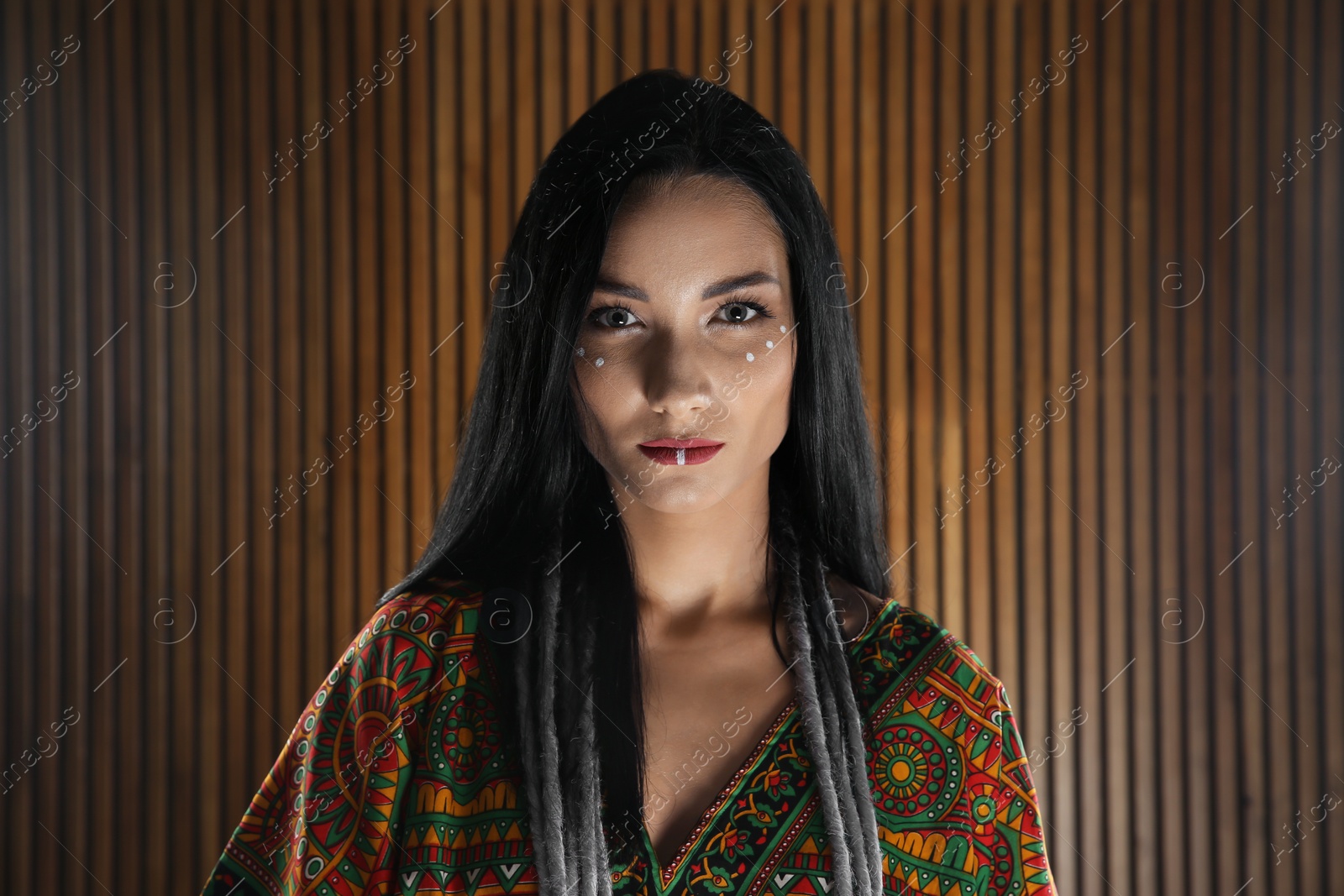 Photo of Portrait of young hippie woman with boho makeup in stylish outfit on wooden background