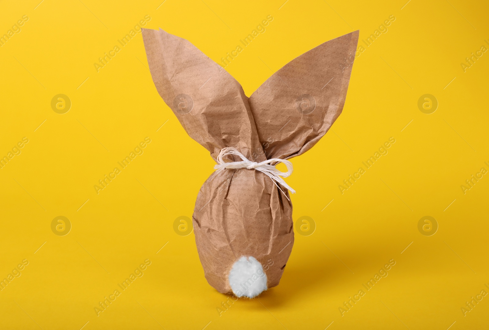 Photo of Easter bunny made of kraft paper and egg on yellow background