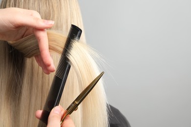 Photo of Hairdresser combing and cutting client's hair on light grey background, closeup. Space for text