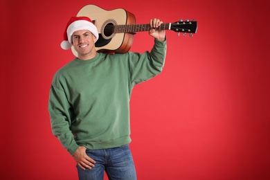 Photo of Man in Santa hat with acoustic guitar on red background, space for text. Christmas music