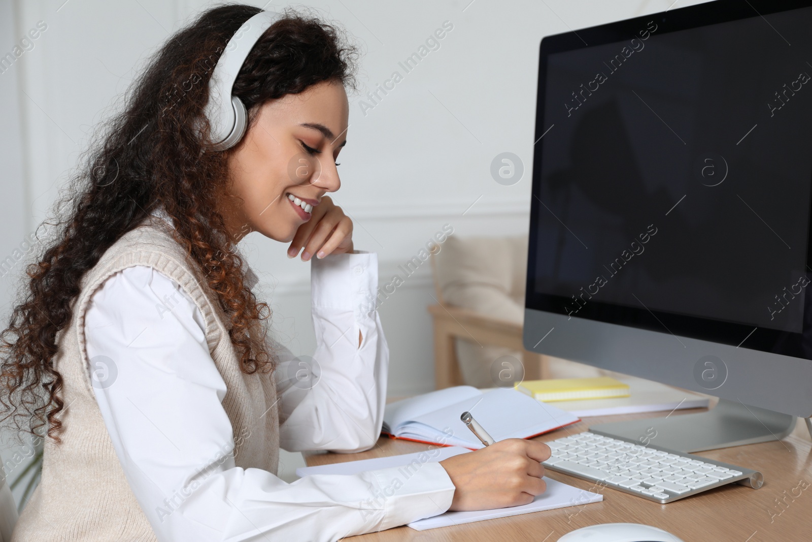 Photo of African American woman with headphones using modern computer for studying at home. Distance learning