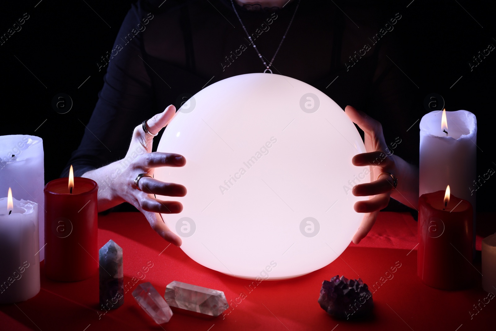 Photo of Soothsayer using glowing crystal ball to predict future  at table in darkness, closeup. Fortune telling