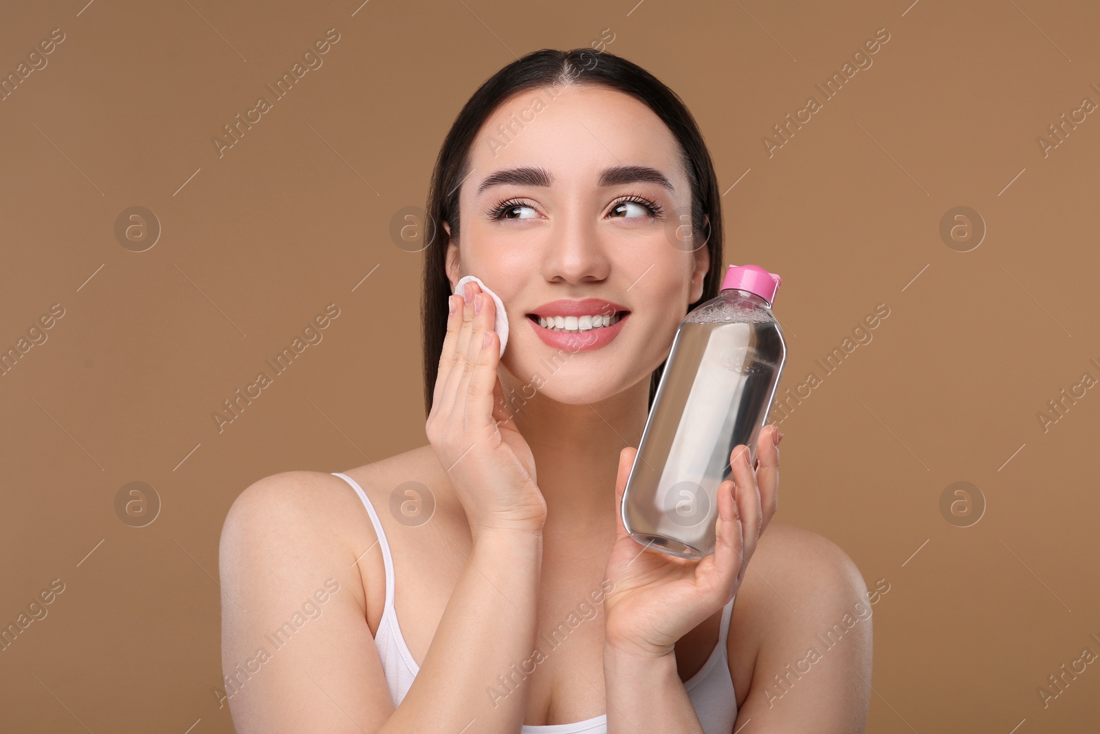 Photo of Beautiful woman removing makeup with cotton pad on beige background