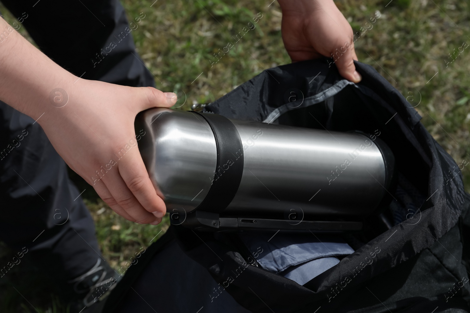 Photo of Hiker putting thermos into backpack outdoors, closeup