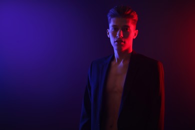Photo of Sexy young man on dark background in neon lights. Space for text